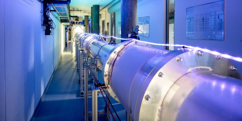 Image of a long metallic pipe extending down a hallway lit in blue.